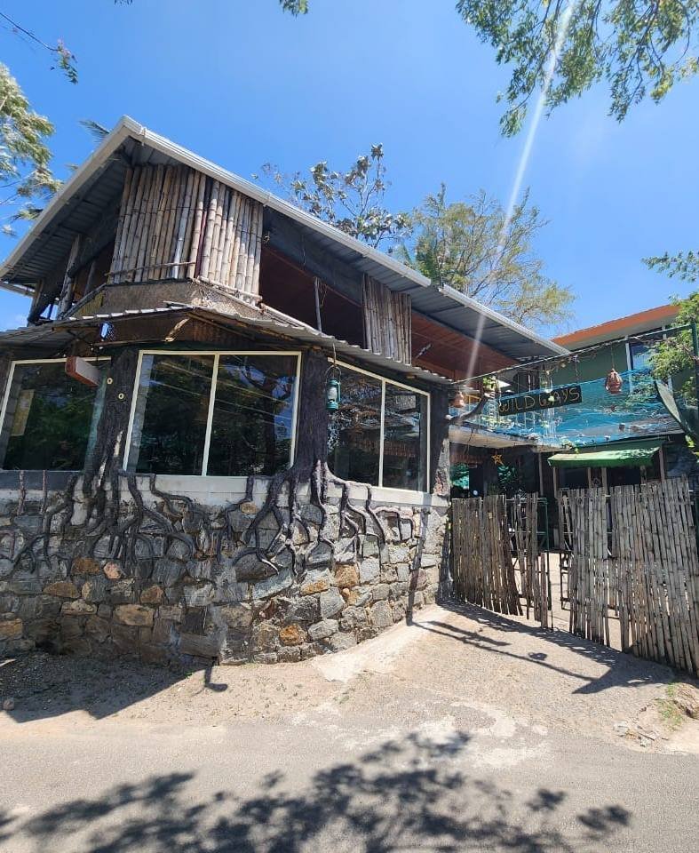 Wild Ways homestay building with a stone base and wooden upper floor under a blue sky